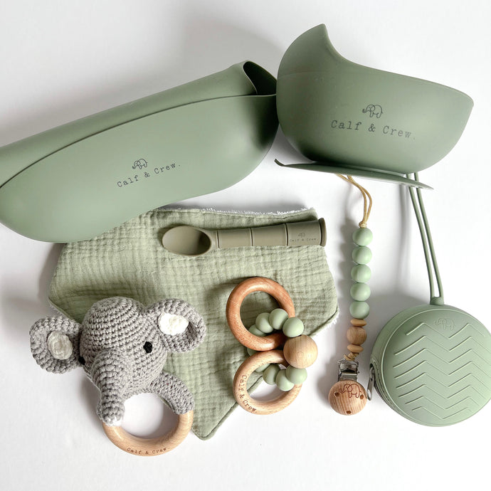 Folded silicone bib and suction bowl, soother case and spoon in sage colour, a wooden silicone ring teether, a silicone dummy clip in mint colour, a grey crochet elephant rattle with a sage muslin bib